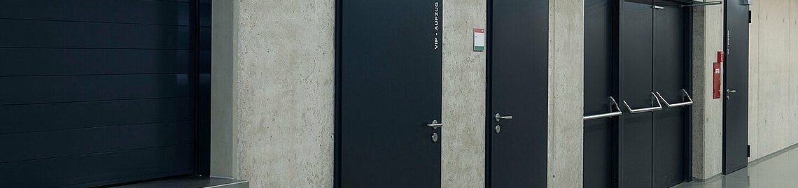 Portes coupe-feu de secours Couloir avec plusieurs portes noires et un mur en béton.